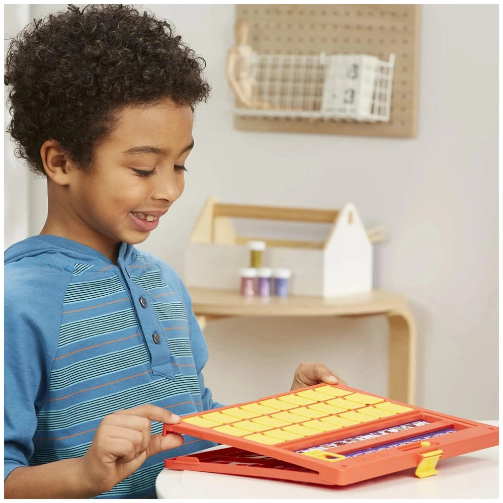 Hasbro Wer Ist Es board game displayed on a white table with a young boy in a blue and orange striped shirt holding yellow cr