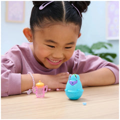 Hatchimals Alive Blind Box Surprise Mini Figures Toy sits on a table as a young girl with dark hair smiles while playing.