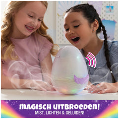 Hatchimals Alive Mystery Hatch Pufficorn interactive plush toy sits on a table as two girls play and smile in a colorful indo