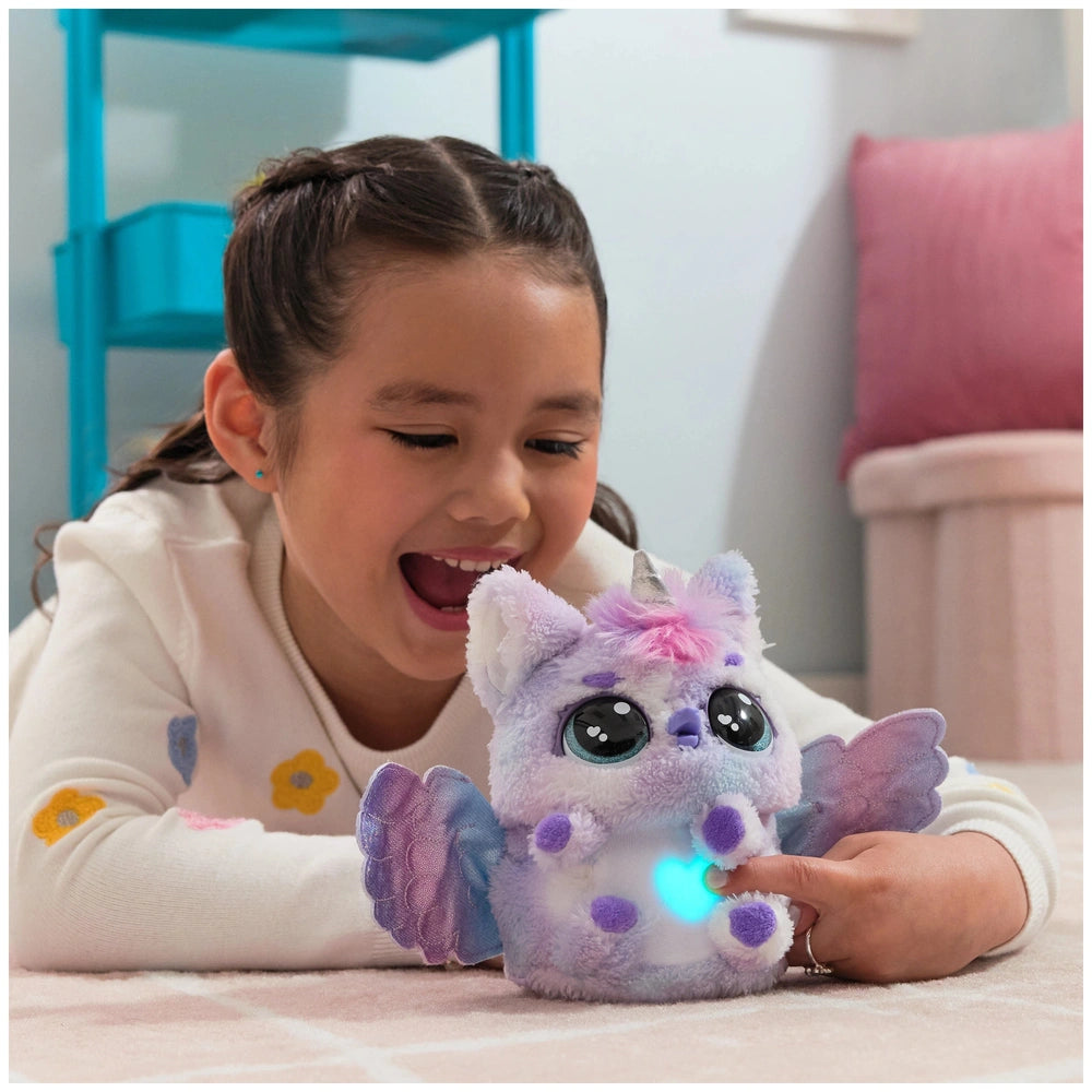 A young girl smiles while holding a purple and white Hatchimals Alive Pufficorn plush with a glowing blue light on its chest.