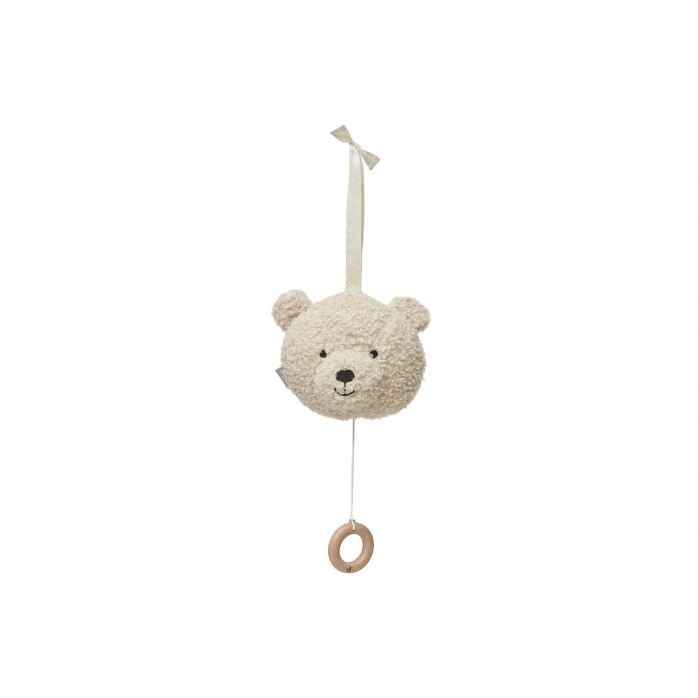 Light beige teddy bear stuffed animal hanging from a string attached to a dark brown circular object against a plain white ba