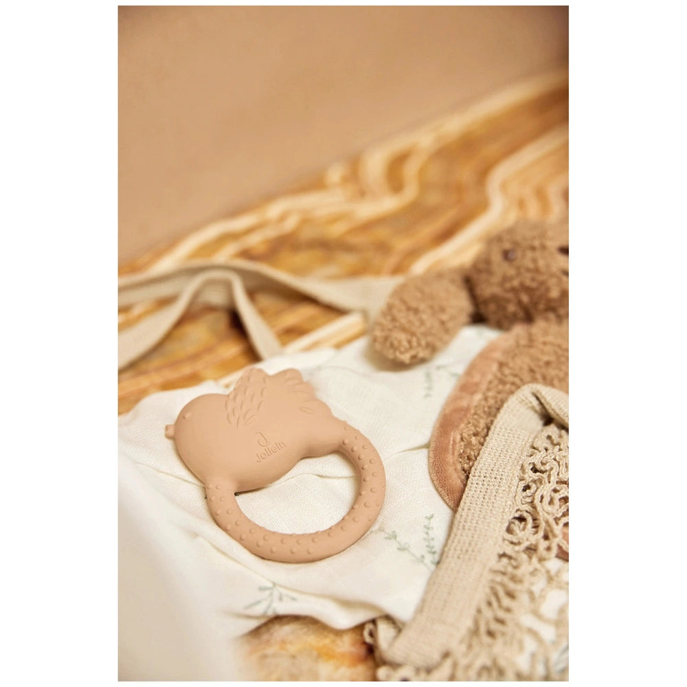 Jollein pacifier cloth bunny in brown rests on a beige knitted blanket atop a natural wood surface.