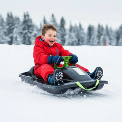 Child in red snowsuit on black KHW Snow Fox sled with green attachment in a snow-covered landscape.