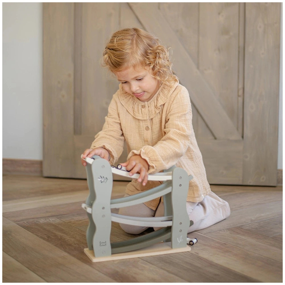 Label-Label-Car-Slider-Baby-Activity-Toy with a young child in a light-colored room, sitting on a wooden floor and rug.