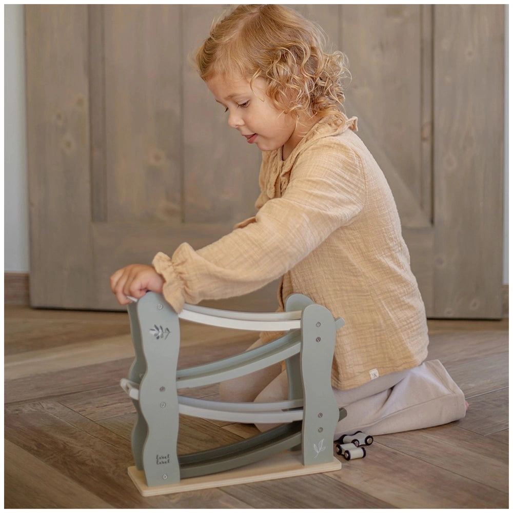 Label-Label Car Slider baby activity toy on wooden floor with a blonde child in beige attire sitting on a gray chair.