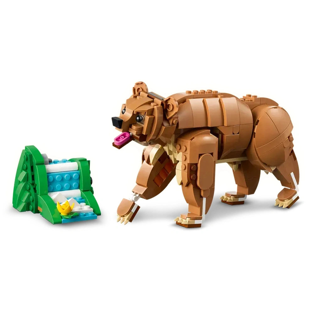 LEGO Creator brown bear with a pink tongue, standing beside a green base featuring a blue and white waterfall and a yellow flower.