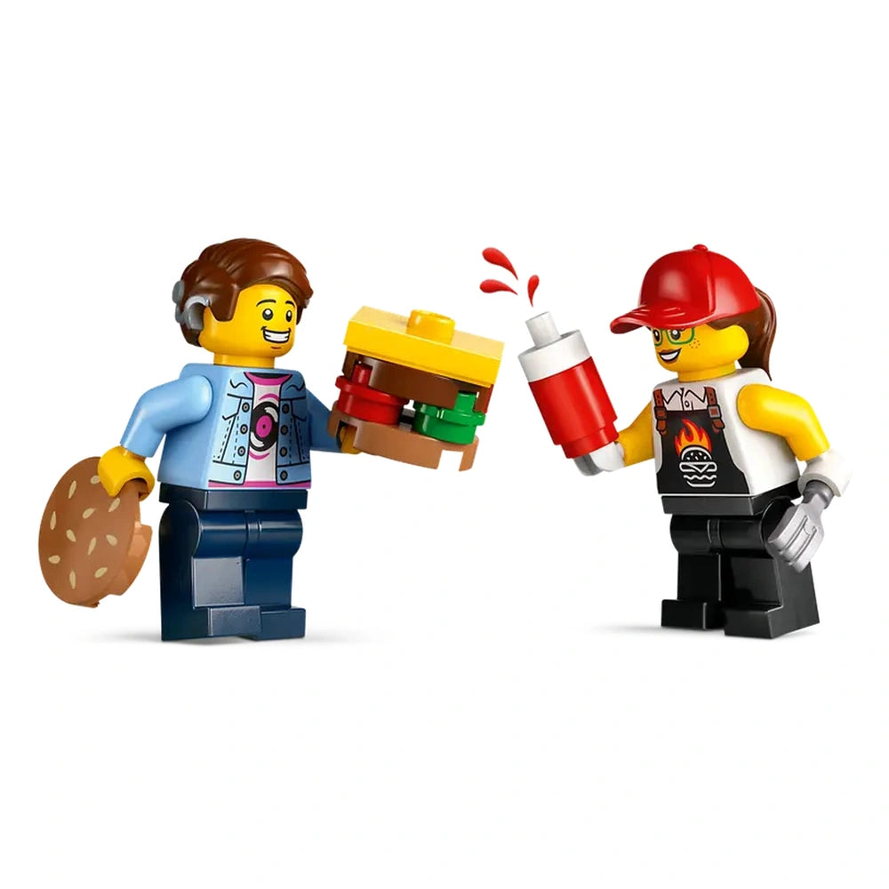 Two LEGO minifigures interact at a burger truck, one holding a colorful burger and the other dispensing ketchup, showcasing a fun fast-food scenario.