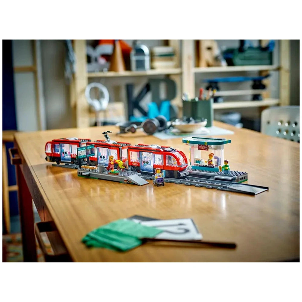 LEGO® City Downtown Streetcar and Station set featuring a vibrant red streetcar, minifigures, and a coffee shop at the station on a wooden table.