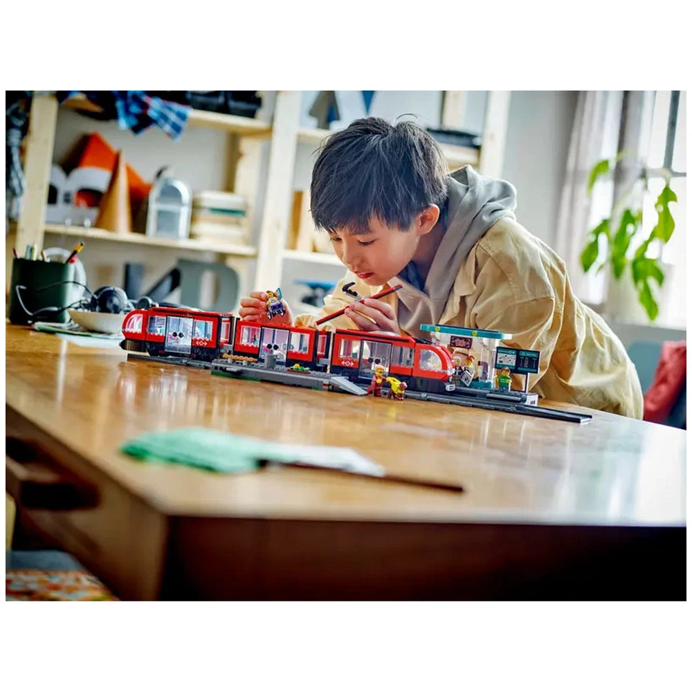 A child plays with the LEGO® City Downtown Streetcar set on a wooden table, focusing on the vibrant streetcar and station elements.