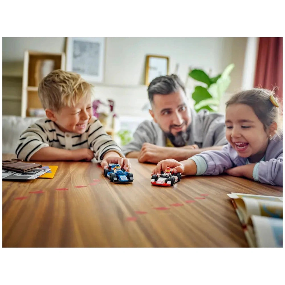 Two children and a man excitedly play with LEGO® F1 race car models on a wooden table, smiling and reaching out as the cars roll.