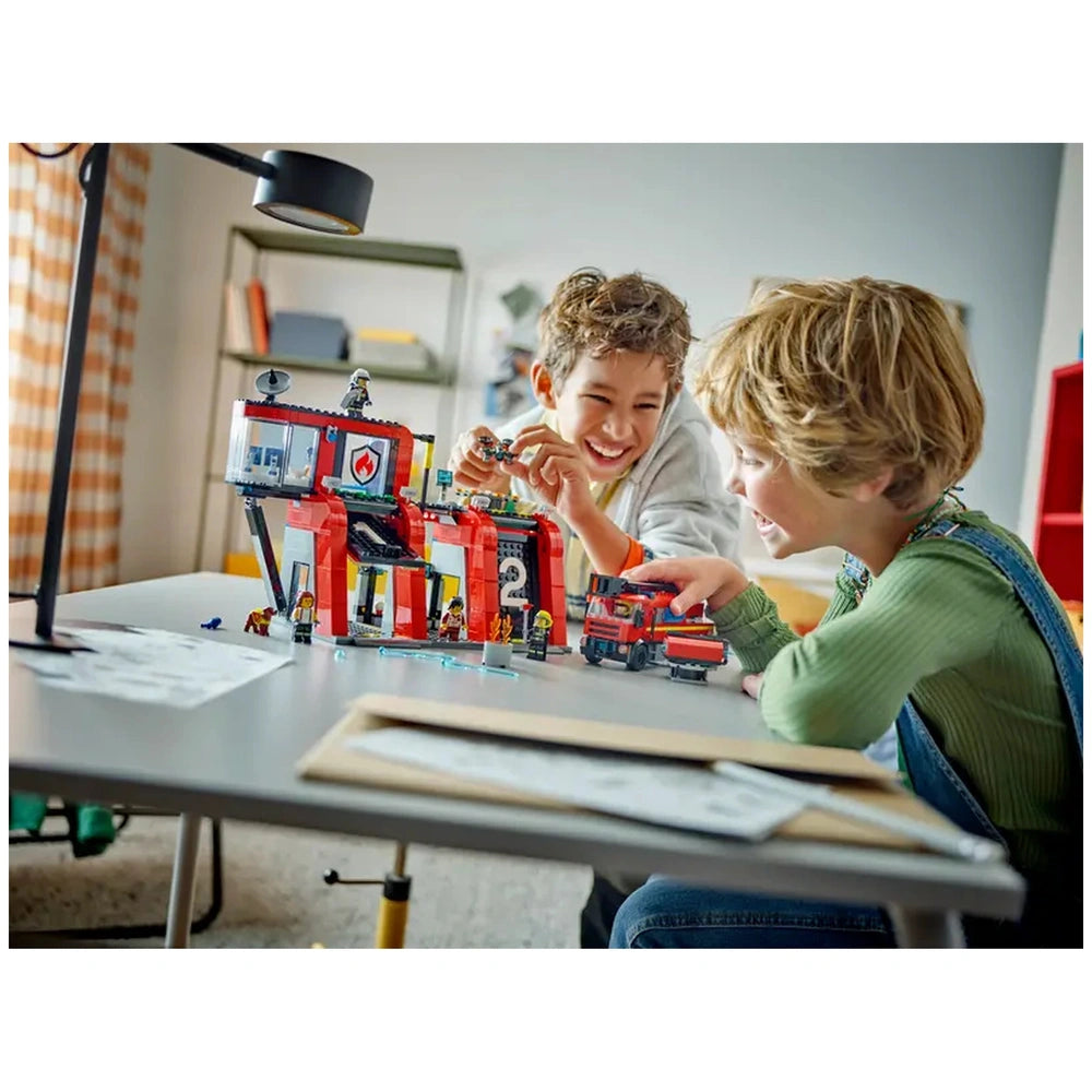 Two children joyfully playing at a table, interacting with the LEGO City Fire Station set, featuring a red fire truck and firefighter minifigures.