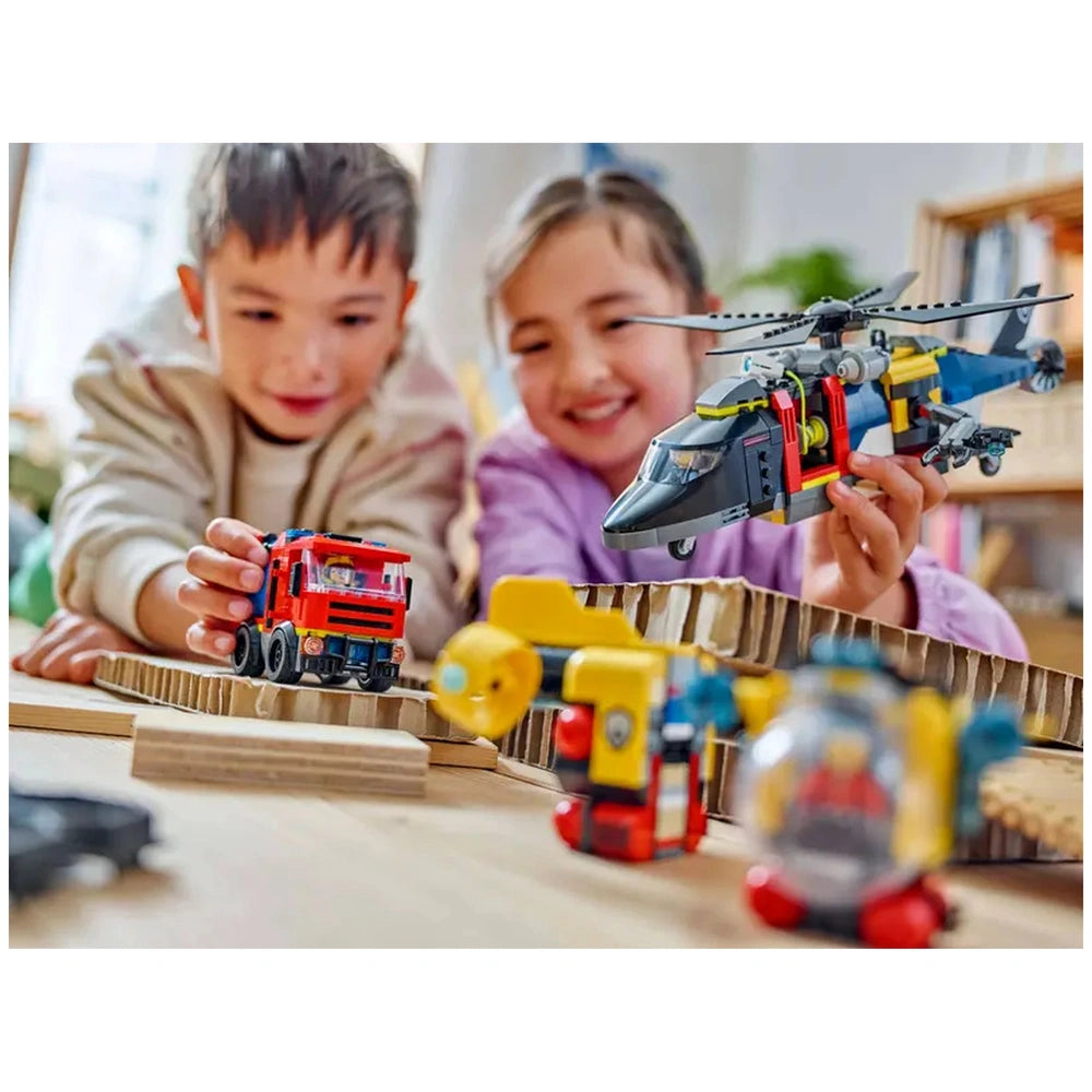 Two children are playing with LEGO® models on a wooden surface. One child holds a red fire truck while the other smiles, holding a helicopter. Various colorful toy models, including a yellow submarine, are scattered around them, showcasing an adventurous scene.