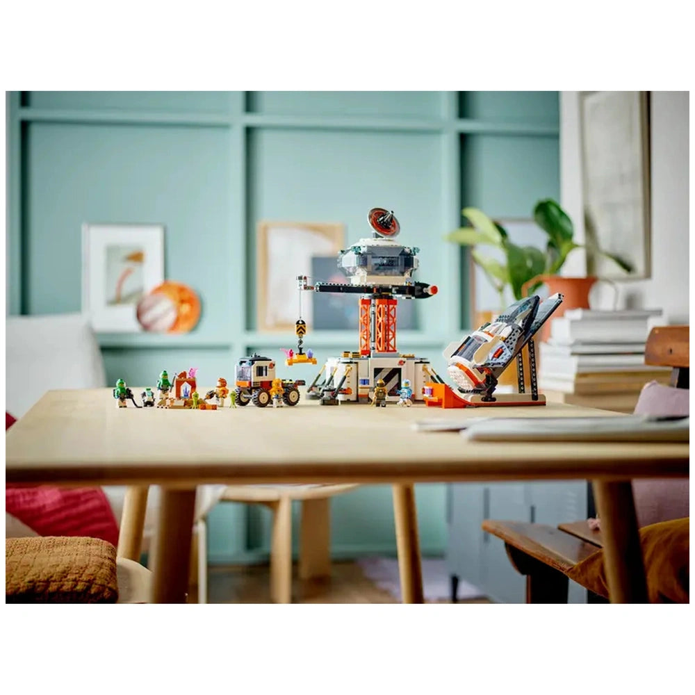 LEGO City Space Base and Rocket Launchpad set displayed on a wooden table, featuring a colorful space station, vehicles, and astronaut minifigures against a light green background.