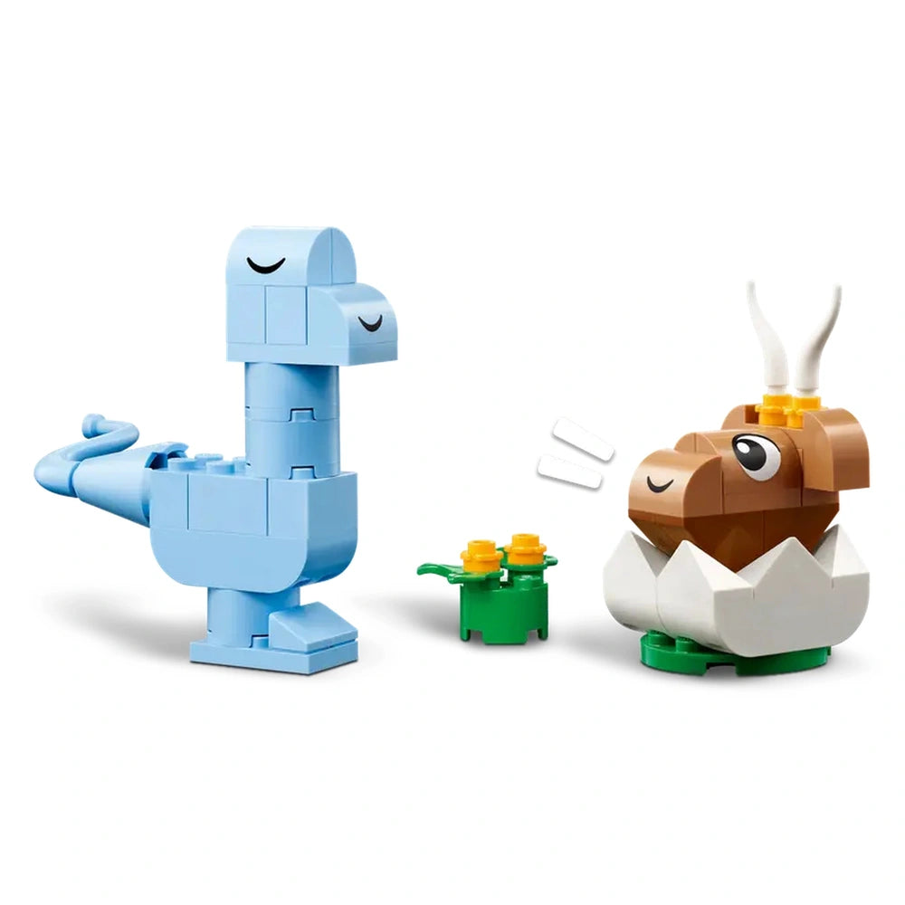 Colorful LEGO dinosaur figures, including a blue dinosaur and a brown baby T. rex in an egg, alongside a small green plant with yellow flowers.