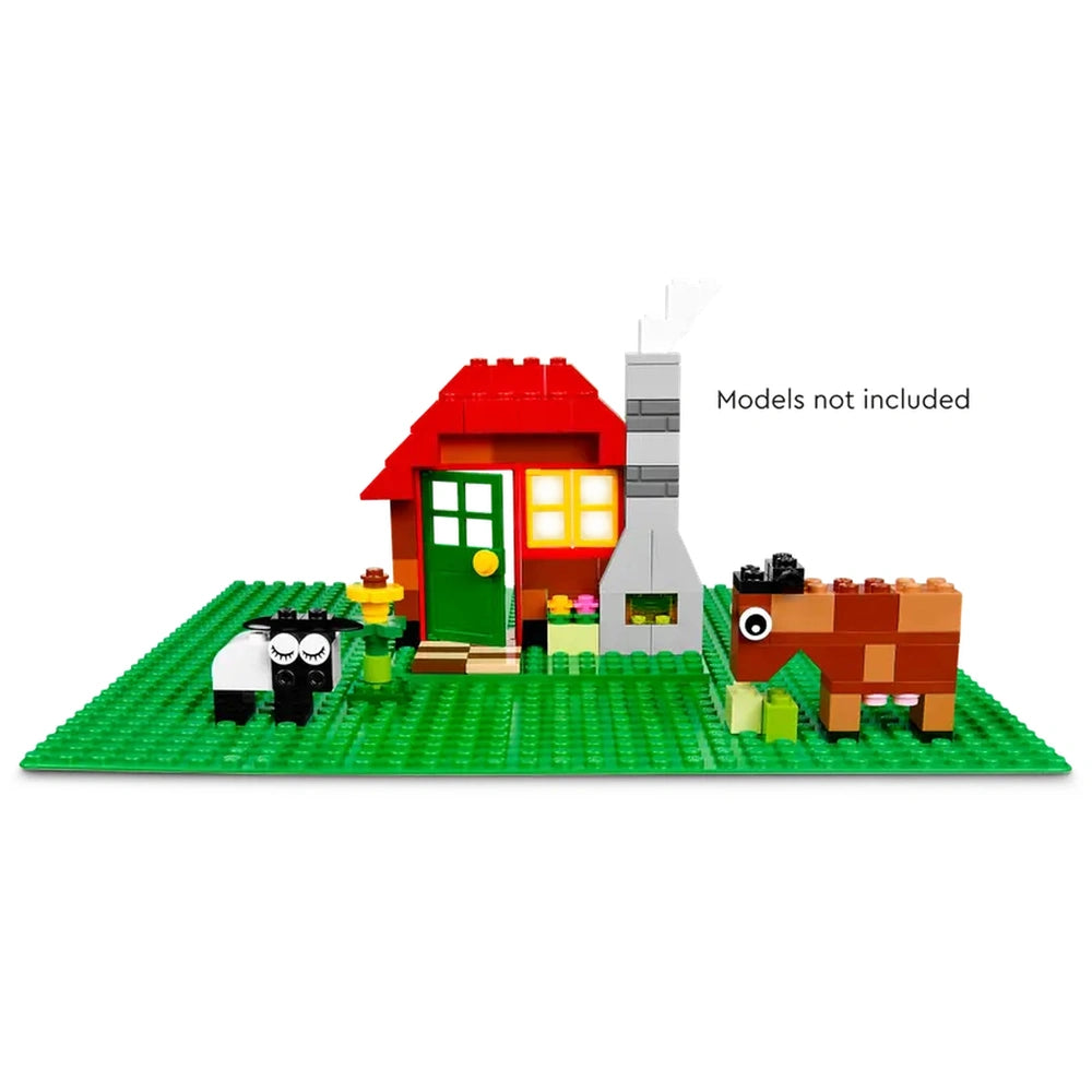 LEGO Classic Green Baseplate featuring a colorful toy house with a red roof, green door, and a stone chimney. Two playful animals, a black and white sheep and a brown horse, are visible on the lush green baseplate, surrounded by colorful flowers and greenery.
