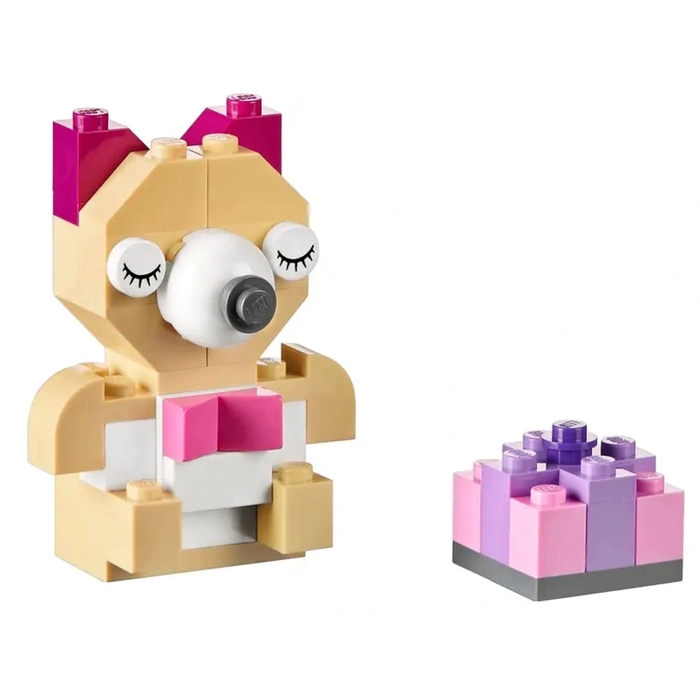 Colorful LEGO bear figure with a white snout and pink bowtie, next to a small purple and pink gift box.