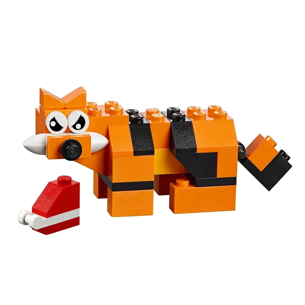 Orange and black LEGO construction model of a fox with large eyes and a white snout, beside a red block resembling a Santa hat.