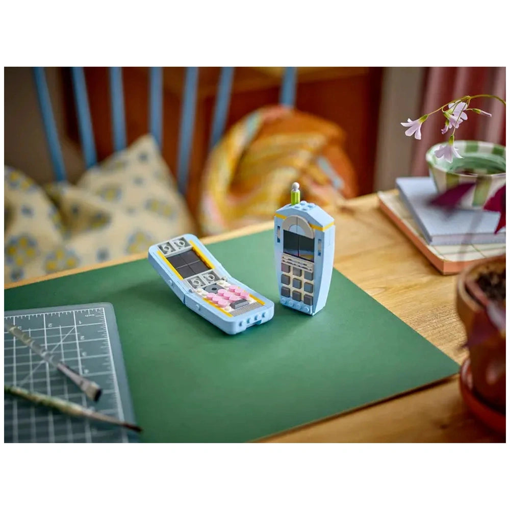 LEGO Creator 3in1 Retro Telephone set featuring a 1960s rotary phone and a 1980s phone, displayed on a green surface with craft tools nearby.