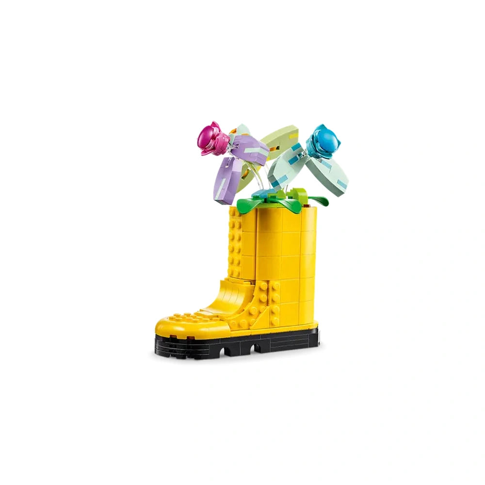 Bright yellow LEGO® construction boot filled with colorful flower toys—pink, purple, and blue—on a green base, showcasing creativity and fun.