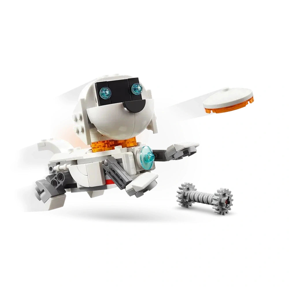 A playful white LEGO robot dog with a black face and bright eyes leaps joyfully, holding a flying disc in the air. A small gray bone lies nearby, emphasizing the adventurous theme.
