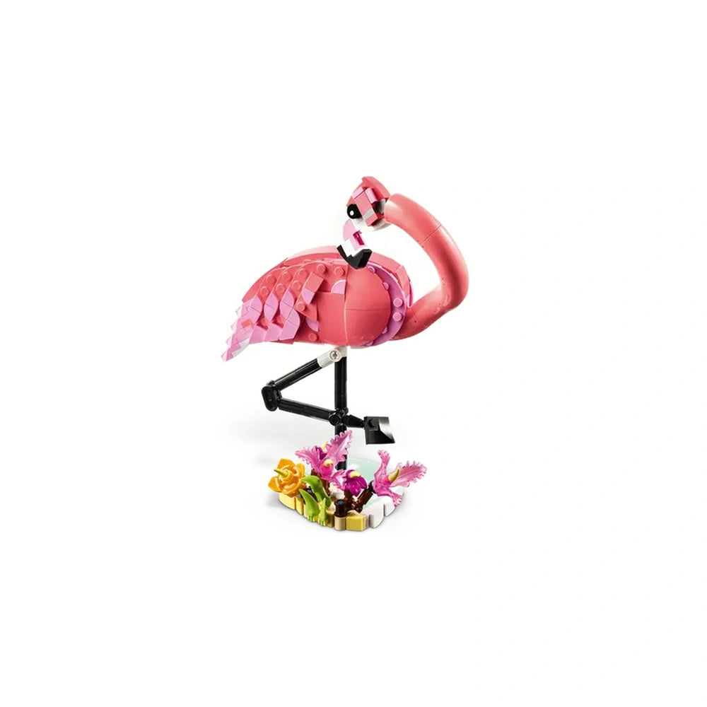 A vibrant pink LEGO flamingo stands on one leg atop a colorful base of flowers and plants, showcasing posable features for imaginative play.