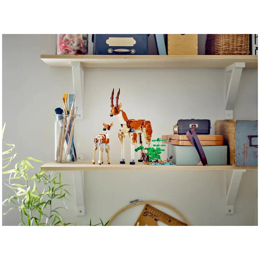 Colorful LEGO Creator Wild Safari animal models, including a giraffe and a smaller animal, displayed on a wooden shelf with art supplies.