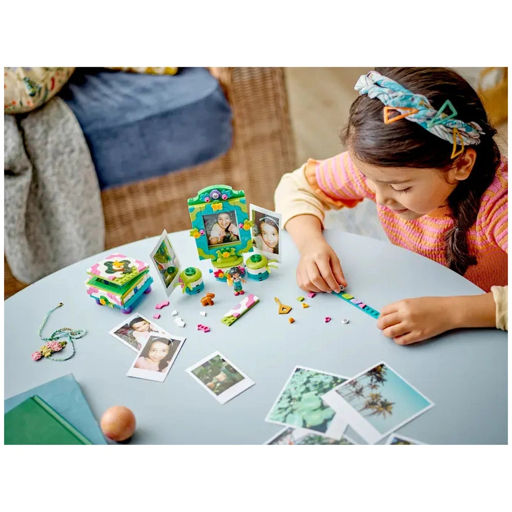 A child assembling the colorful LEGO® Disney Encanto Mirabel’s Photo Frame and Jewelry Box set, surrounded by small photo frames and a bracelet.