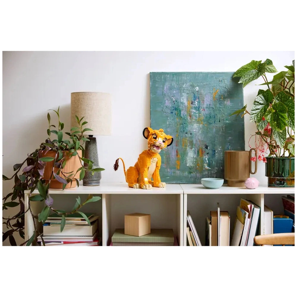 LEGO Disney Young Simba figure displayed on a shelf, surrounded by plants, a lamp, and an abstract painting, creating a cozy decor.
