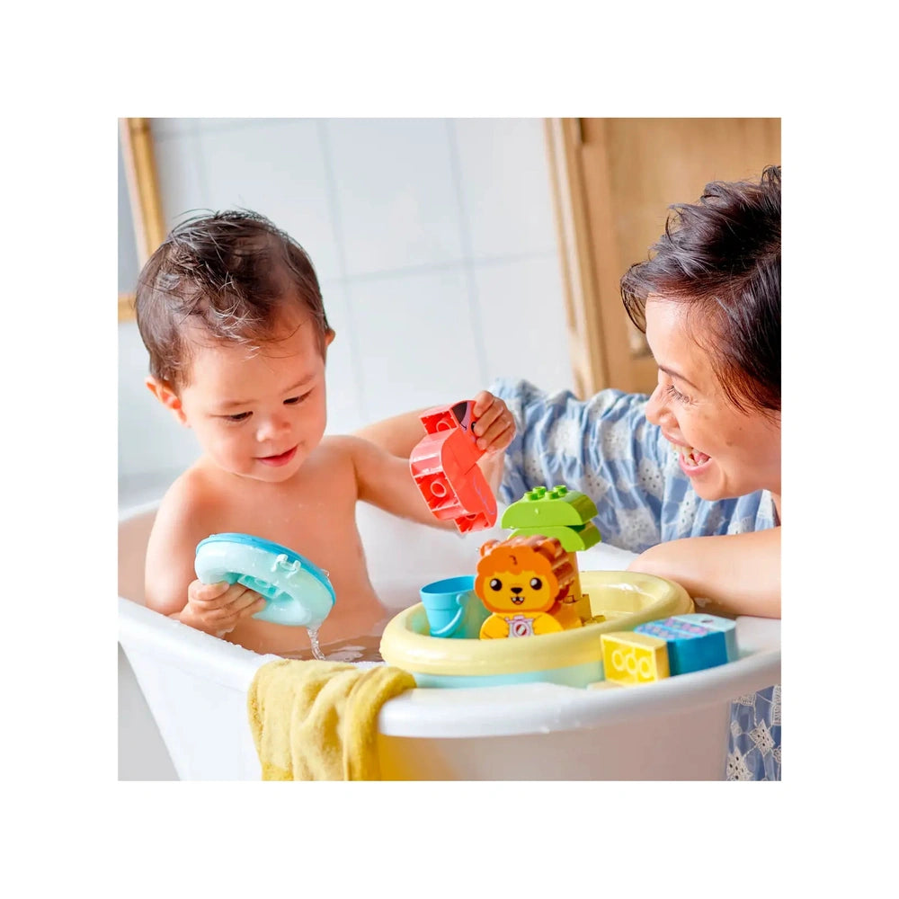 A happy toddler in a bathtub plays with colorful LEGO® DUPLO® floating animals, including a lion and a flamingo, while a smiling adult engages in the fun.
