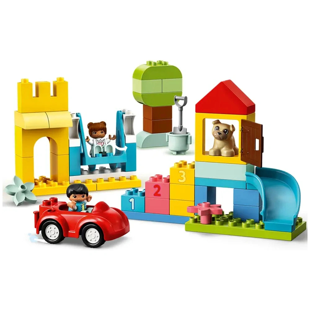 Colorful LEGO® DUPLO® Deluxe Brick Box set featuring a red toy car, a swing, a slide, and building elements like a castle and a tree.