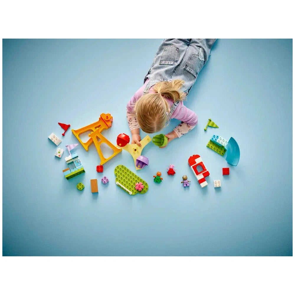 A young child lies on a light blue surface, engaged with colorful LEGO® DUPLO® pieces, including a yellow Ferris wheel, small figures, and a green slide.