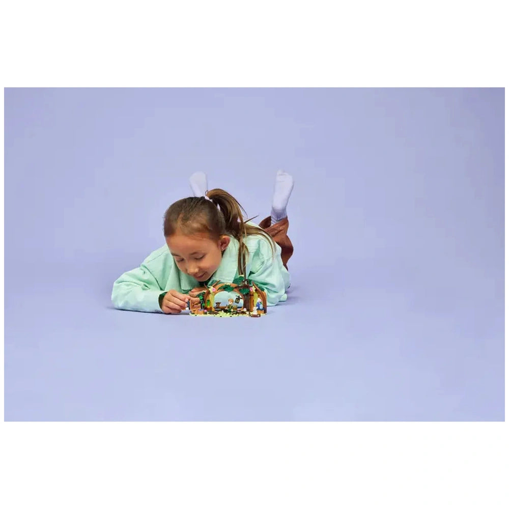 A child lying on their stomach, intently focused on LEGO Elphaba's Retreat set, surrounded by a soft purple background.