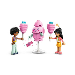 Two LEGO Friends minidolls, one in a striped shirt holding pink cotton candy and the other in orange shorts, beside a cheerful pink cotton candy machine. Bright colors enhance the playful scene, evoking creativity and fun.