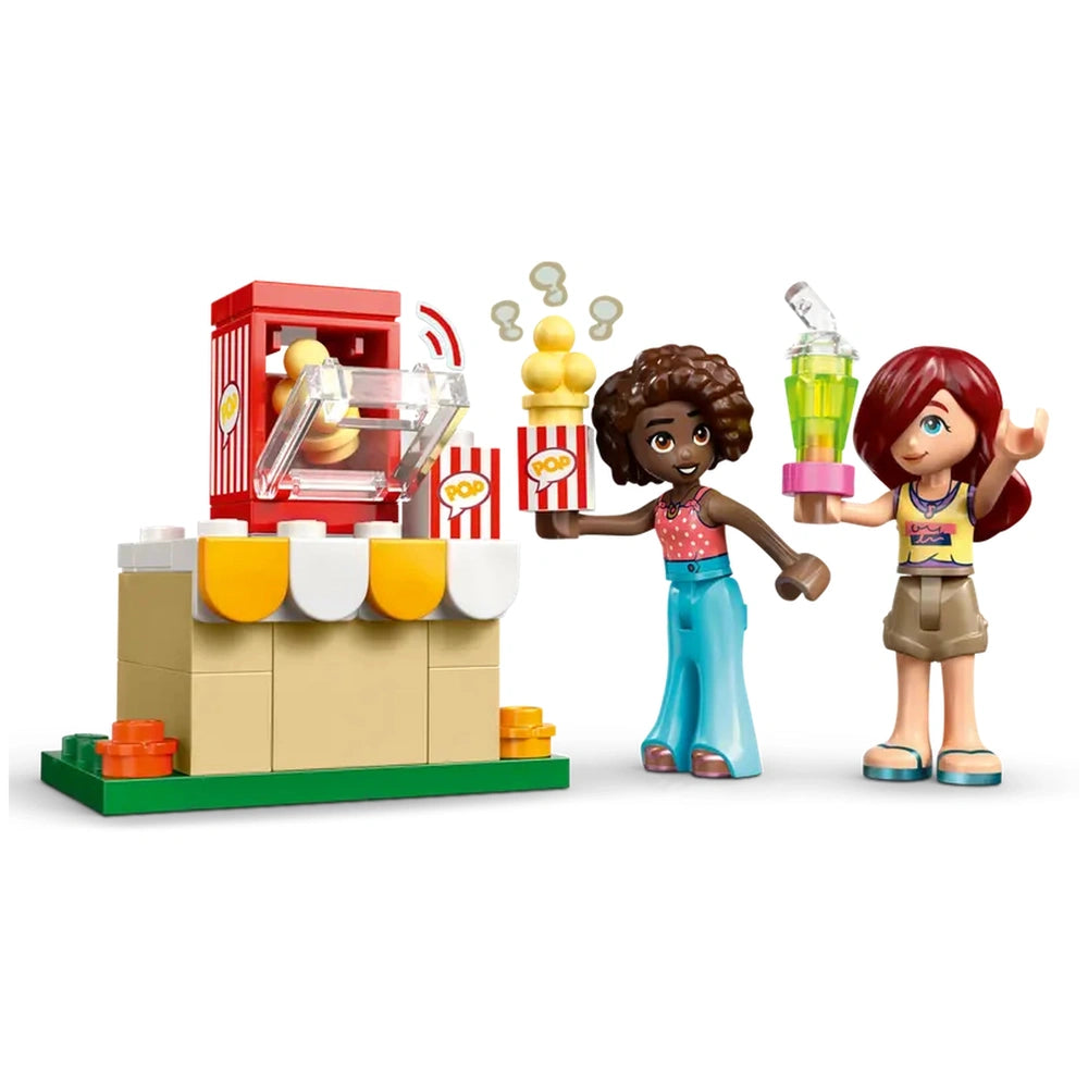 Two LEGO Friends minidolls, one holding popcorn and the other a drink, stand beside a popcorn machine with movie-themed accessories.
