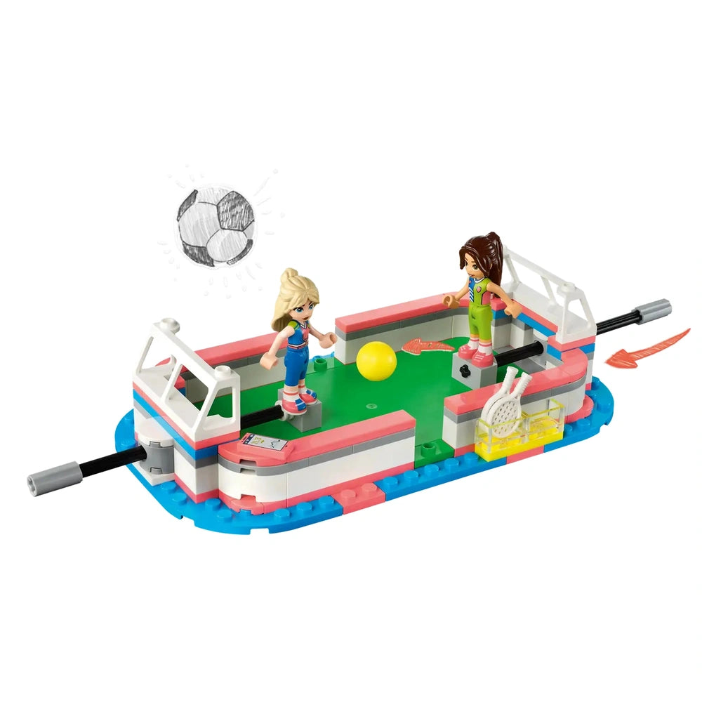 Two mini-dolls on a colorful LEGO® Friends Sports Center playset, with a soccer ball and sports equipment on a vibrant green field.