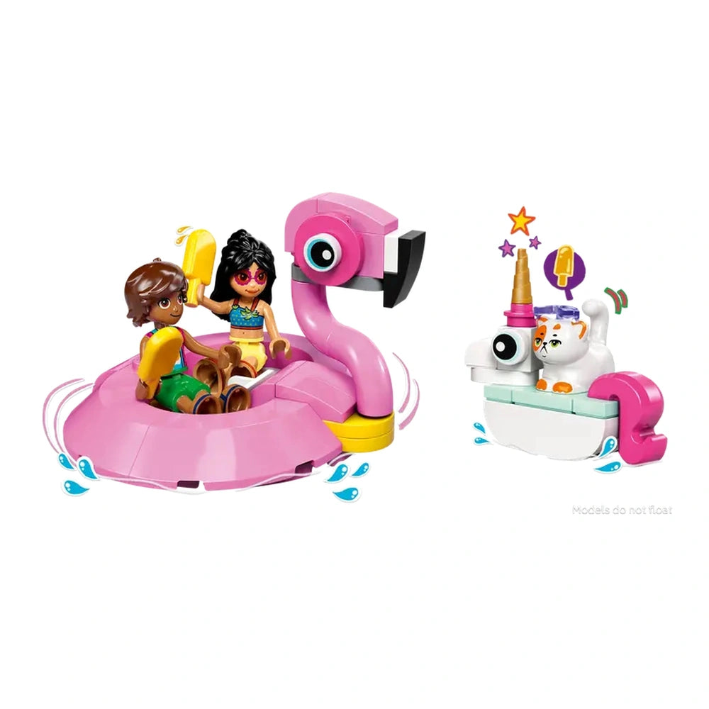 Two LEGO Friends minidolls, Leo and Liann, sit on a large pink flamingo floatie, smiling and holding popsicles. Next to them is a smaller white unicorn floatie with Churro the cat figure, adorned with a horn and colorful accessories. Water splashes around the floaties, enhancing the playful pool party scene.