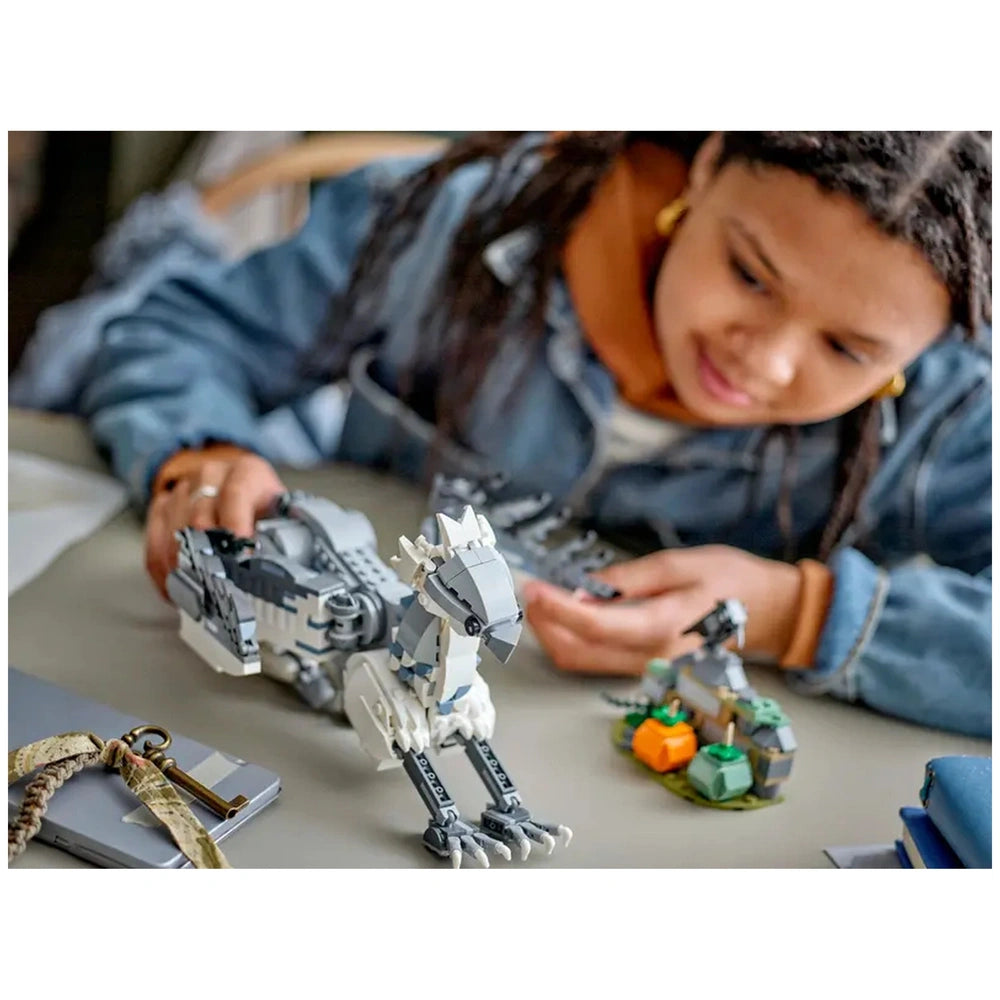 A child in a denim jacket focuses on building a LEGO Harry Potter Buckbeak model, with a small section of Hagrid's yard featuring pumpkins beside them on a table.