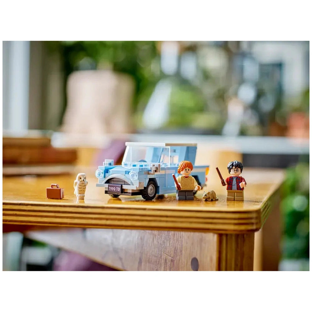 LEGO Harry Potter Flying Ford Anglia set featuring a light blue car, Ron Weasley and Harry Potter minifigures with wands, a suitcase, and Hedwig the owl on a wooden table.