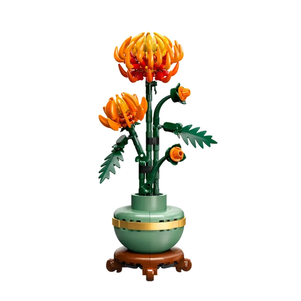 Lego Icons Chrysanthemum construction set, featuring vibrant orange flowers in full bloom and budding stages, with posable green leaves, in a pastel green pot with a golden band, set against a white background.