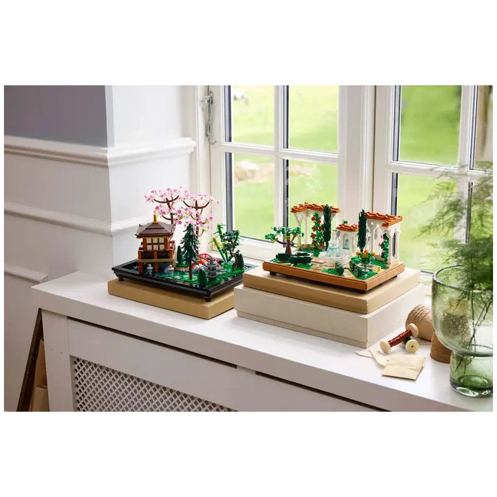 LEGO® Icons Fountain Garden set displayed on a windowsill, featuring a tiered fountain, cherry trees, and charming pergolas surrounded by vibrant flowers.