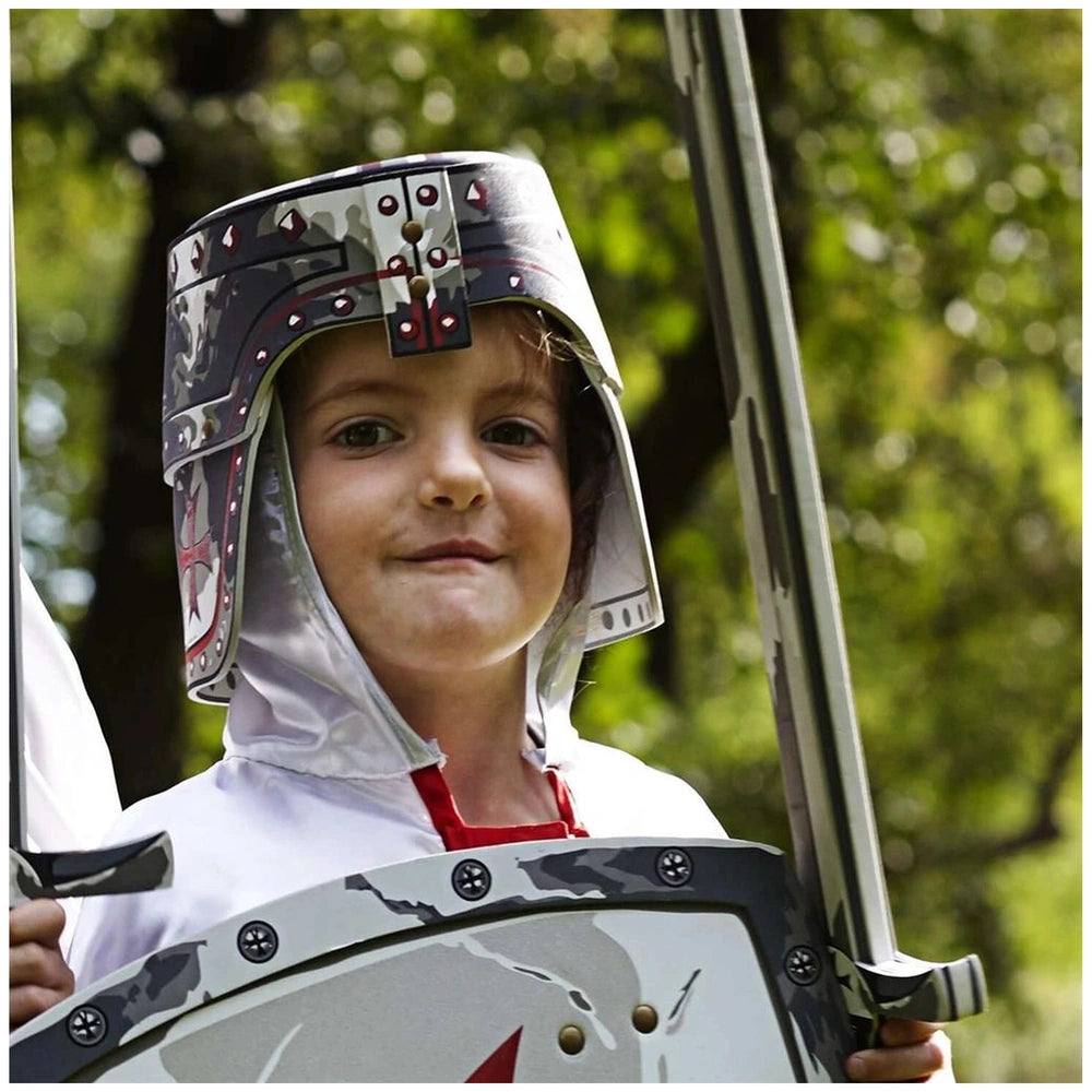 Child dressed as a Maltese knight in a silver and black helmet, holding a metallic shield with a red star and sword.