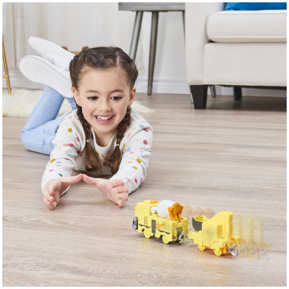 Mighty Express Motorized Train in yellow is played with by a smiling girl in colorful attire on a wooden floor.