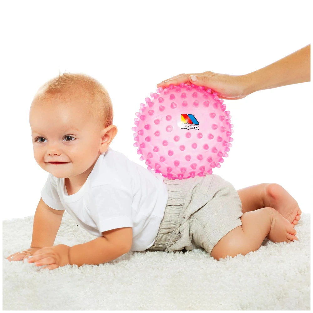 Molto Playsense Sensory Ball in pink, with a smiling baby in a white t-shirt and khaki shorts on a fluffy surface.