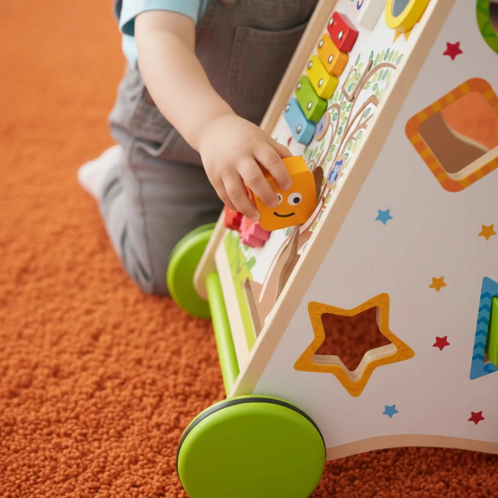New Classic Toys Activity Walker packaging with colorful shapes, pegs, and an orange smiling toy held by a child's hand.