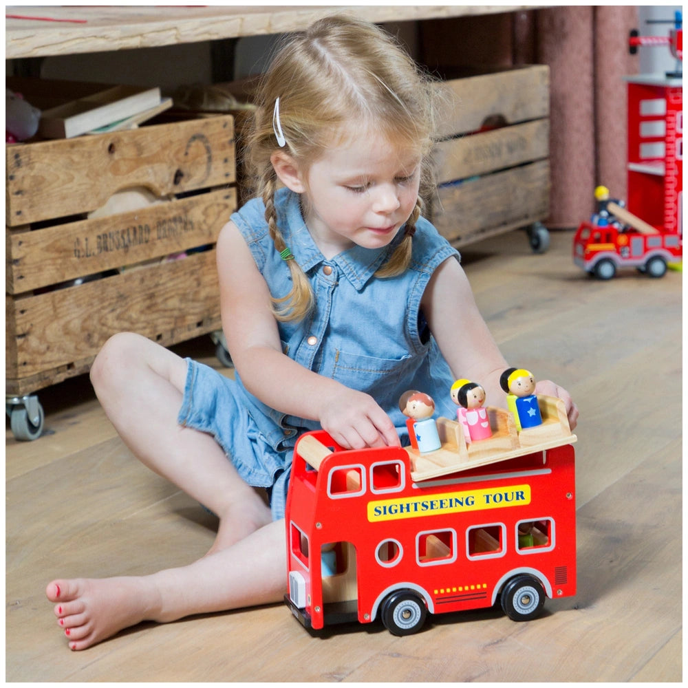 City Tour Bus with 9 Play Figures surrounded by a young girl, wooden crate, and dollhouse on wooden flooring.