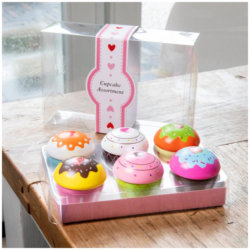 Cupcake assortment in a clear plastic gift box featuring six colorful, decorated cupcakes on a wooden table.