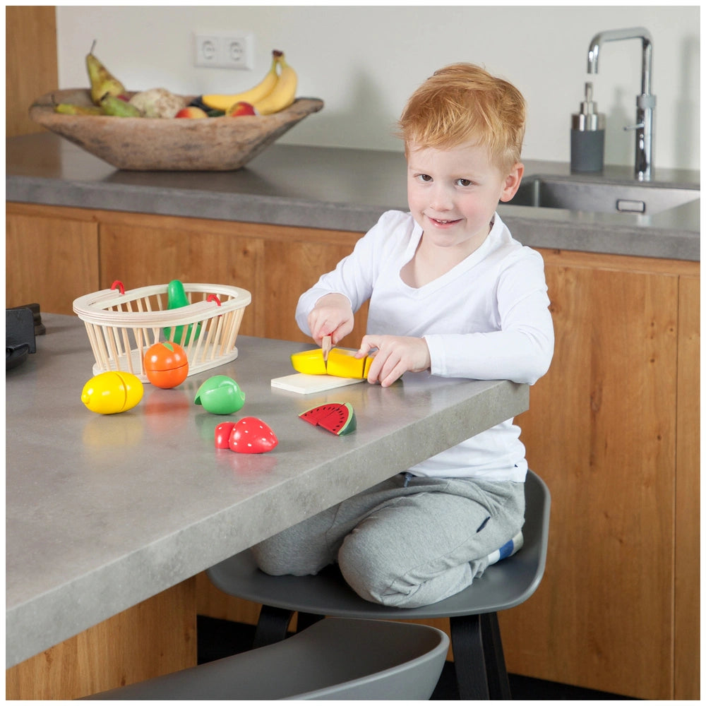 a bright kitchen with a smiling child in a white shirt and gray sweatpants, engaged with a colorful fruit bowl.