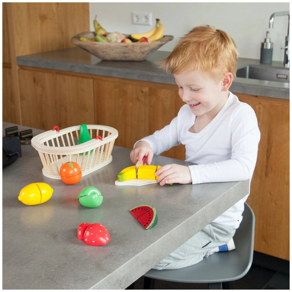 New Classic Toys fruit basket set with a young child playing on a wooden kitchen countertop surrounded by plastic containers.