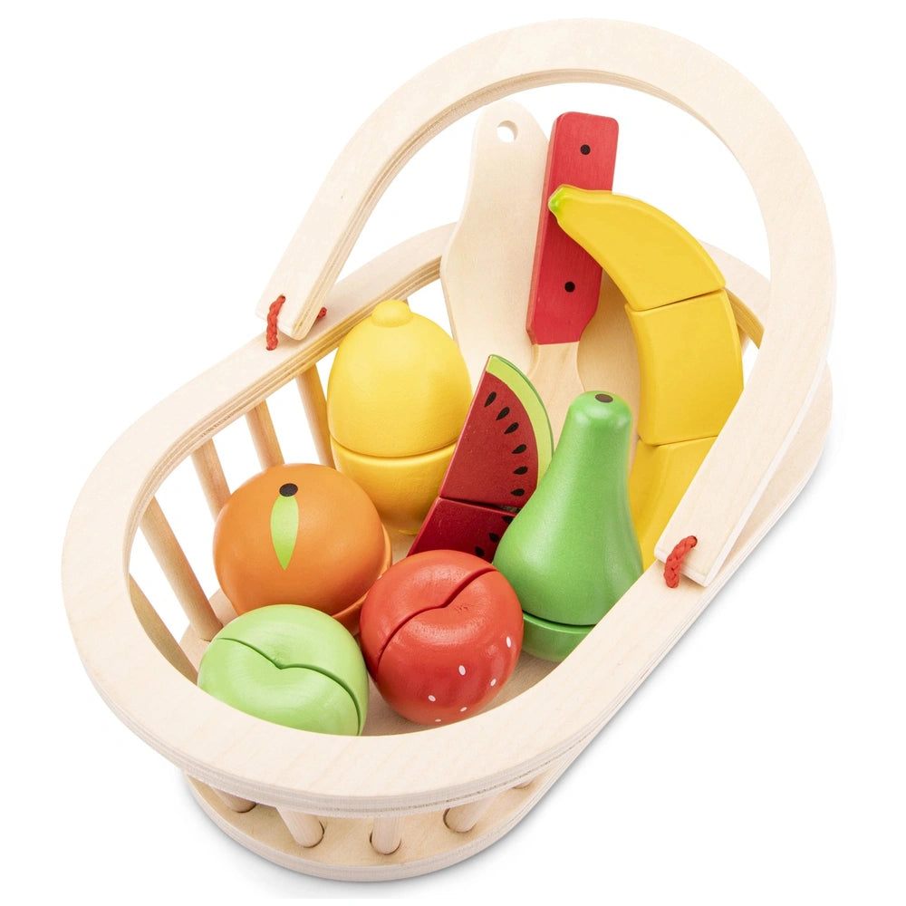 Wooden basket filled with colorful plastic fruits and vegetables including tomatoes, watermelons, oranges, bananas, and bell 