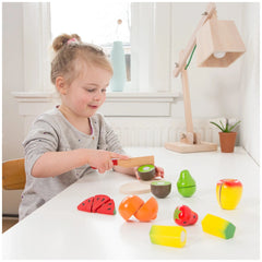 Young girl playing with New Classic Toys fruit box cutting set on a wooden table, featuring colorful plastic toy components.